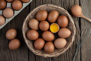 Fresh brown eggs in a wicker basket with a cracked egg yolk on a rustic wooden table – a protein-rich healthy food.