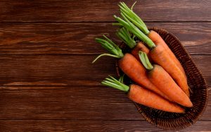 Fresh carrots in a basket on a wooden background – a nutritious and natural healthy food rich in vitamins.